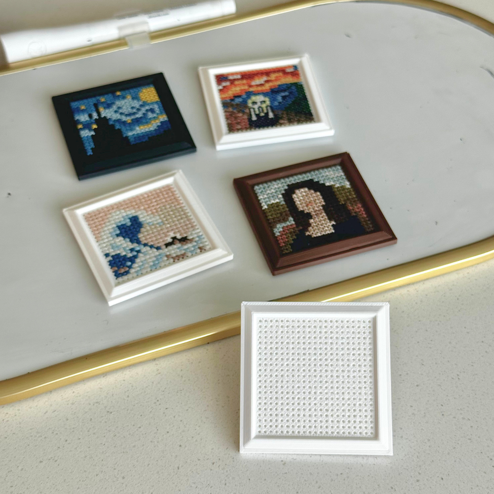 Five small framed canvas prints arranged on a light gray surface with a gold metal edge. Four frames show completed artwork: a blue night-sky scene, a multicolor horror portrait, a blue-and-white scene, and a dark portrait.